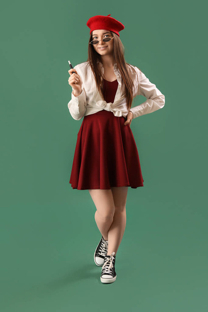 Стильная молодая женщина с одноразовой электронной сигаретой на зеленом фоне - Фото, изображение