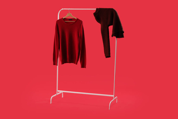 Rack with knitted sweaters on red background - Foto, afbeelding