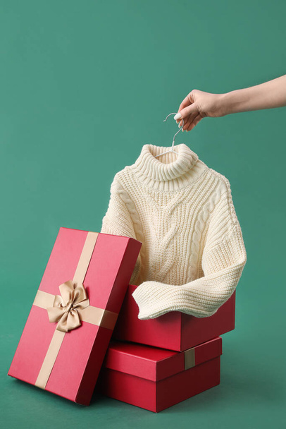 Woman with knitted sweater and Christmas gifts on green background - Photo, Image