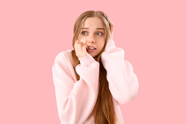Молода жінка в светрі кусає цвяхи на рожевому фоні
 - Фото, зображення
