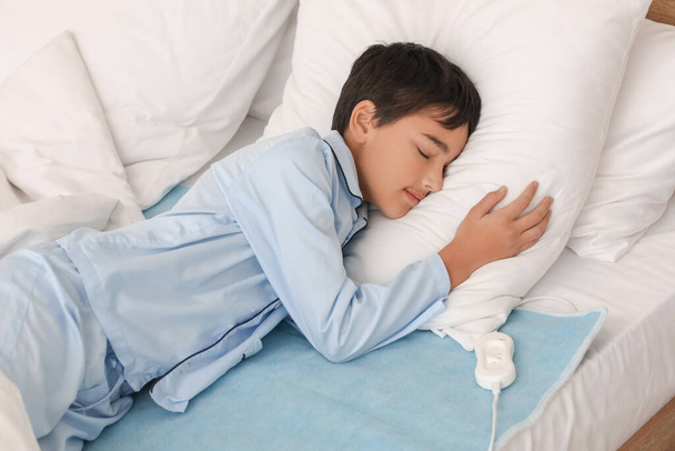 Little boy sleeping on electric heating pad in bedroom - Foto, afbeelding