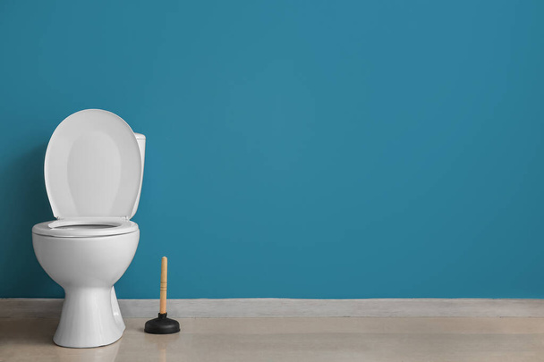 Ceramic toilet bowl and plunger near blue wall - Fotoğraf, Görsel