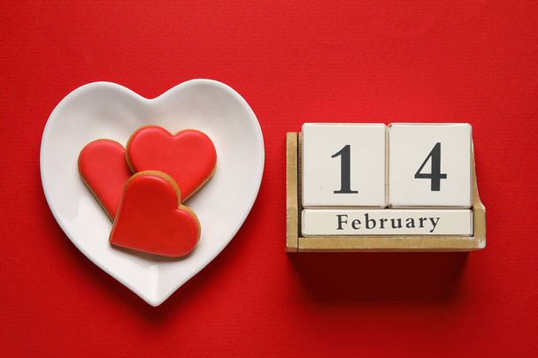 Plate of tasty heart shaped cookies and  calendar with date 14 FEBRUARY on red background. Valentines Day celebration - Foto, Bild