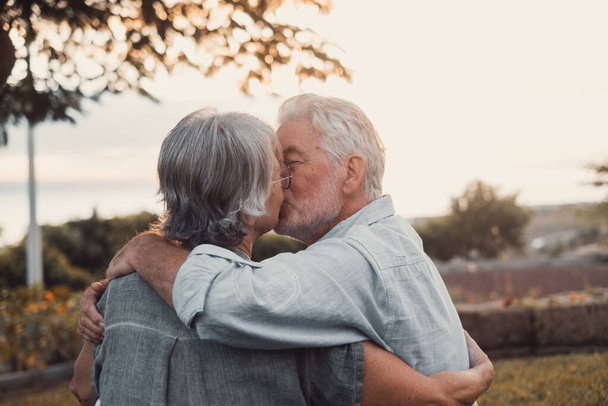 Head shot close up portrait happy grey haired middle aged woman snuggling to smiling older husband, enjoying tender moment at park. Bonding loving old family couple embracing, looking sunset. - Photo, image