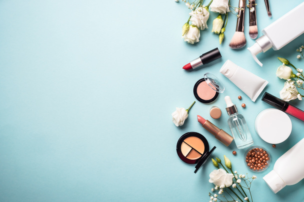 Make up professional cosmetics on blue background. Cream, powder, shadow, brushes with green leaves and flowers. Flat lay image with copy space. - Valokuva, kuva