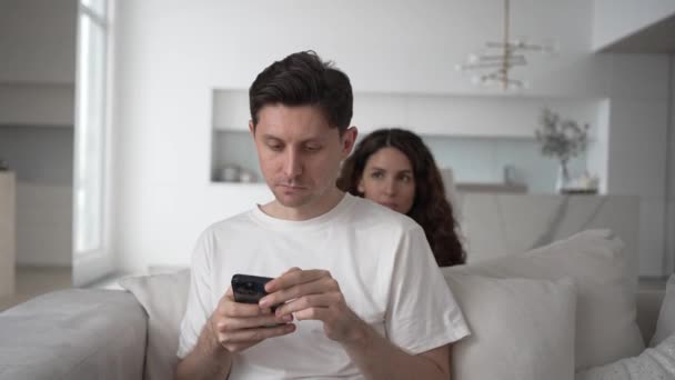 Jealous wife hides behind the sofa and spies on the correspondence in her husbands phone, jealousy and distrust in the family. - Imágenes, Vídeo