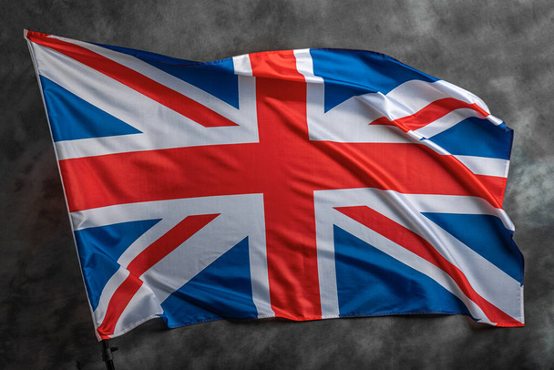 Britische Flagge auf dunklem Hintergrund. Großbritannien-Flagge auf dem Hintergrund einer dunklen Leinwand für ein patriotisches Konzept und nationale Feierlichkeiten. - Foto, Bild