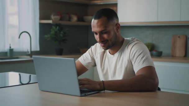 Африканский тысячелетие мужчина многорасовый парень Американский пользователь фрилансер сидит на домашней кухне стол, используя ноутбук, работающий удаленно с компьютерным приложением сервис онлайн ставки игры в чате покупки в Интернете - Кадры, видео