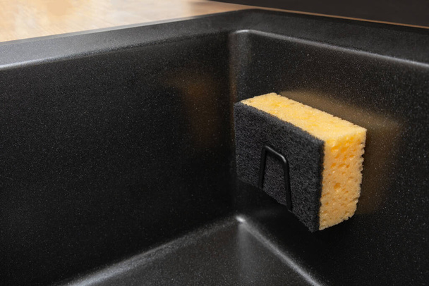 Kitchen organizer holder for a kitchen sponge in a black, clean granite sink. Storage and organization of space, details in the kitchen - Photo, image