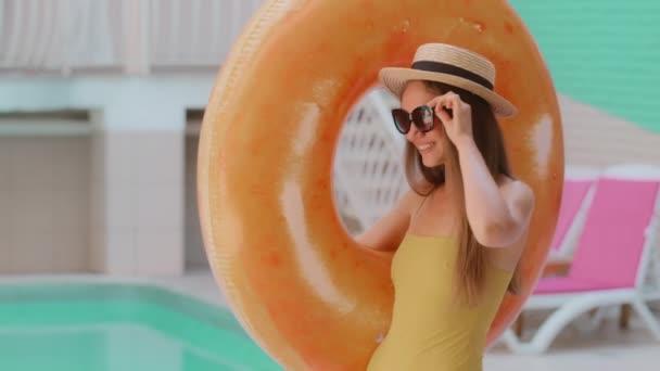 Carefree beautiful stylish woman model Caucasian fashion girl with long hair wears hat and sunglasses carry inflatable ring laughing walk to swimming pool female lady tourist enjoying summer vacation - Filmagem, Vídeo