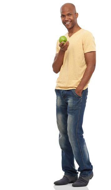 Ξέρεις τι λένε, ένα μήλο την ημέρα. Πυροβολισμός μεγάλου μήκους ενός όμορφου Αφροαμερικανού που στέκεται άνετα και κρατάει ένα μήλο. - Φωτογραφία, εικόνα