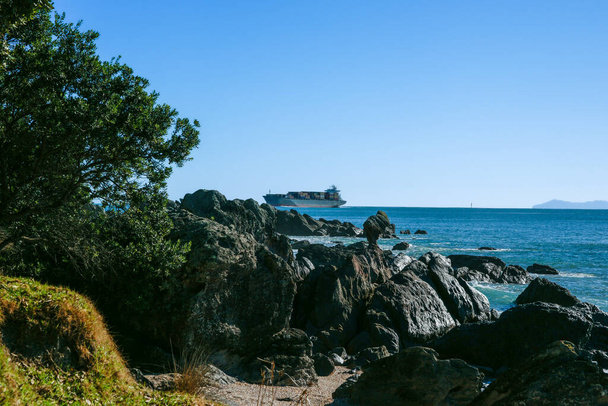 Small container ship passing rocky base Mount Maunganui entering Port of Tauranga. - Foto, immagini