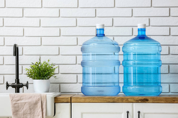 Bottles of clean water and sink on kitchen counter near white brick wall - Fotoğraf, Görsel