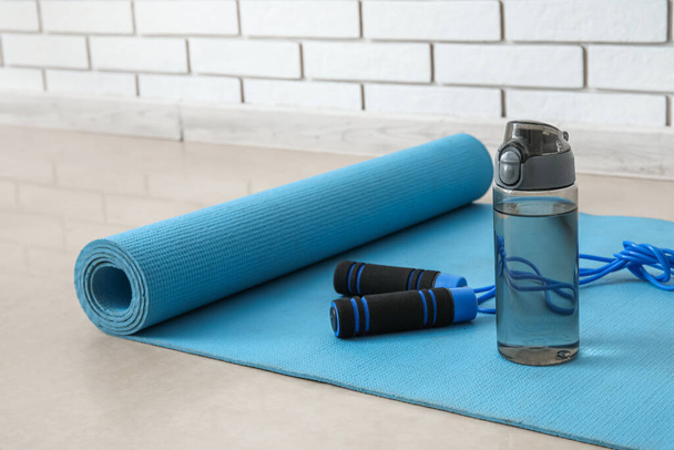 Sports water bottle with skipping rope on mat near white brick wall - Foto, Bild