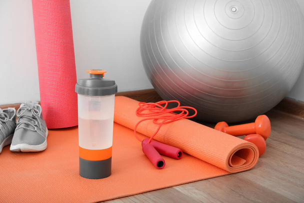 Sports water bottle with equipment and sneakers on mat near light wall - Photo, Image