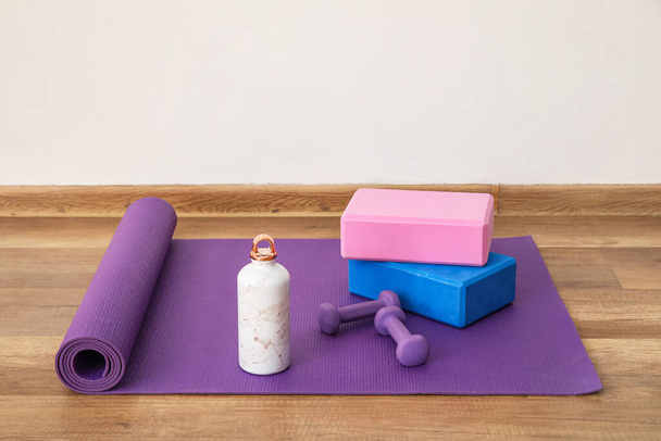 Sports water bottle with equipment on mat near light wall - Photo, Image