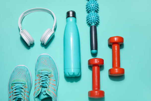 Бутылка спортивной воды с оборудованием, наушниками и кроссовками на цветном фоне - Фото, изображение