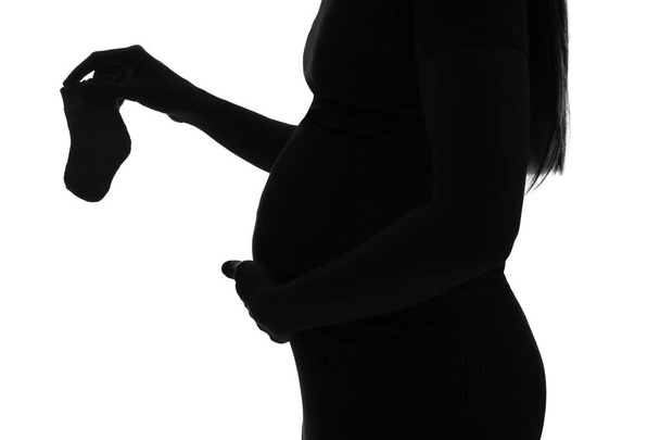 Σιλουέτα της νεαρής εγκύου με κάλτσες μωρό σε λευκό φόντο, closeup - Φωτογραφία, εικόνα