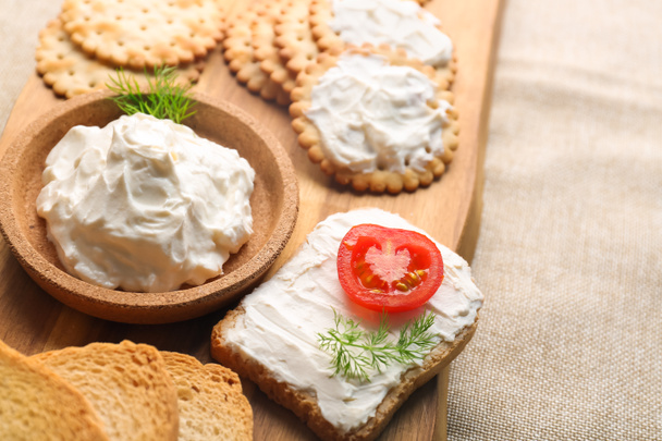 Wooden board with bowl of tasty cream cheese and crackers on table, closeup - Foto, Bild