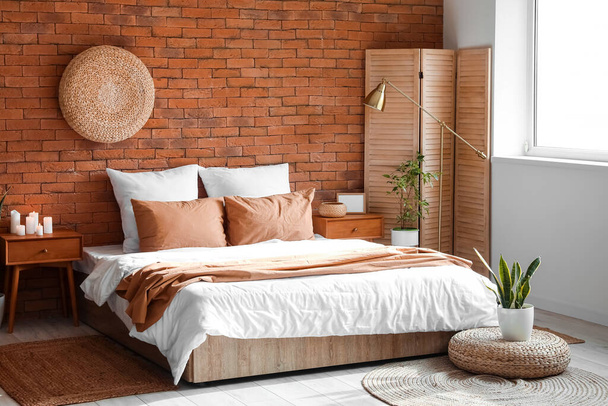 Интерьер современной спальни с деревянными столами, складным экраном и комнатными растениями - Фото, изображение