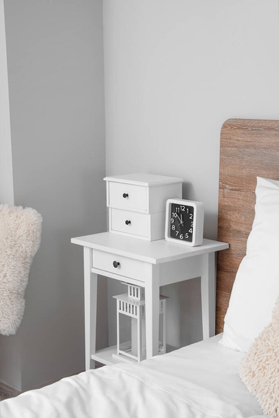 Bedside table with drawers and alarm clock in light bedroom - Foto, afbeelding