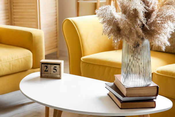 Cube calendar with date SEPTEMBER 25 and pampas grass in vase on table near yellow sofa - Fotoğraf, Görsel