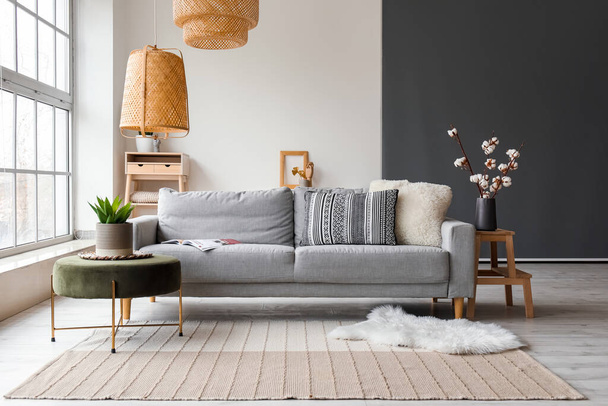 Cozy interior of living room with grey sofa, pouf and fur carpet near window - Photo, Image