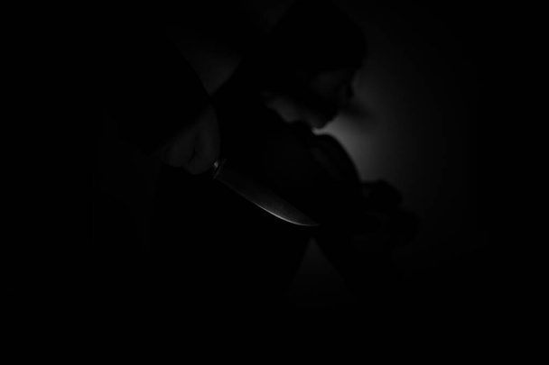 Мужская рука держит нож, а рядом сидит девушка и боится, насилия в отношении людей, преступника и убийцы - Фото, изображение