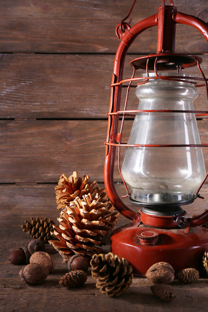 Kerosene lamp with cones ans walnuts on wooden planks background - Foto, Imagen