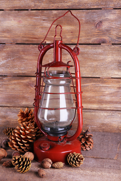 Kerosene lamp with cones ans walnuts on wooden planks background - Photo, image