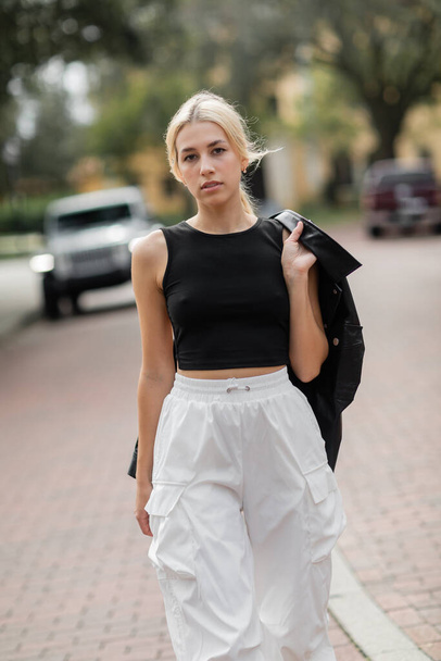 young woman in white cargo pants and tank top walking with black shirt jacket on street in Miami  - Fotografie, Obrázek