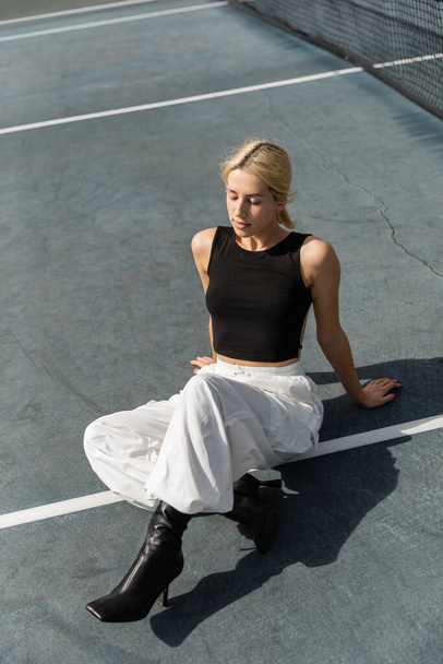 high angle view of young woman in tank top and white cargo pants sitting on tennis court - Fotoğraf, Görsel