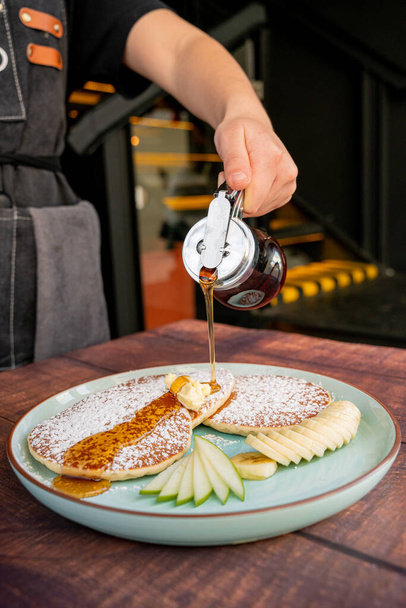 person putting maple syrup on their delicious and fluffy buttery pancakes, accompanied by green apple, perfect breakfast and bruch. - Photo, Image