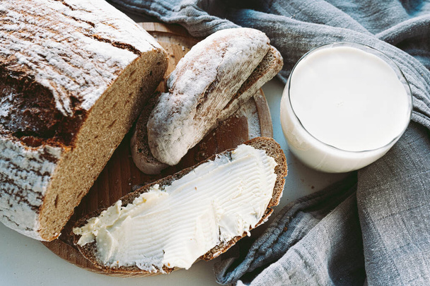 slice of rustic homemade rye flour bread buttered and glass of milk. country food, snack, freshly baked rye bread with butter and milk - Foto, afbeelding