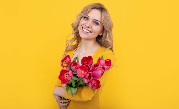 χαρούμενο νεαρό κορίτσι με ανοιξιάτικα λουλούδια τουλίπας σε κίτρινο φόντο. - Φωτογραφία, εικόνα