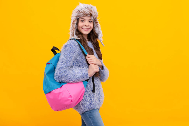 コピースペース、学校と黄色の背景にバックパック付きセーターやイヤーフラップの帽子の幸せな子供. - 写真・画像