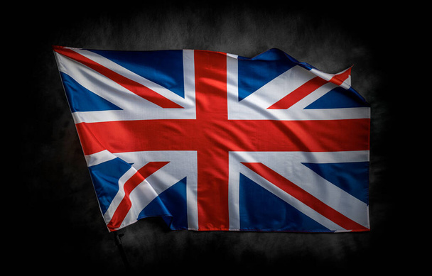 暗い背景に英国の国旗。愛国的な概念と国民のお祝いのための暗いキャンバスの背景に英国の旗. - 写真・画像
