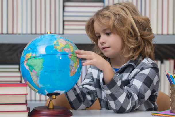 School pupil looking at globe in library, geography lesson. School child studying in classroom at elementary school. Kid studying on lesson in class at elementary school - Foto, afbeelding