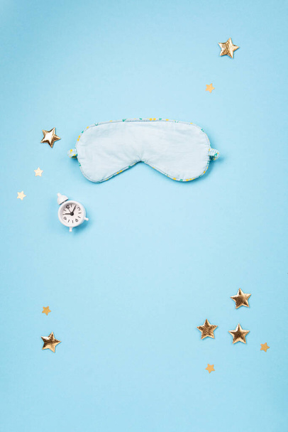 World Sleep day observed on March. Quality of sleep, good night, insomnia, relaxation concept. Sleeping mask, golden stars and white alarm clock on blue background. Flat lay, top view - Foto, Bild