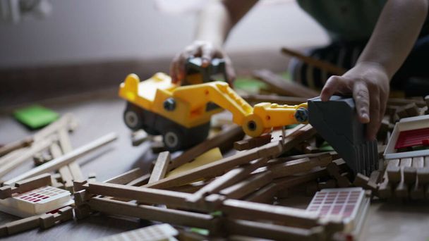 Niño destruyendo juguete casero de madera con pequeño tractor bulldozer. Un niño destructor jugando en casa en la sala de juegos - Foto, Imagen