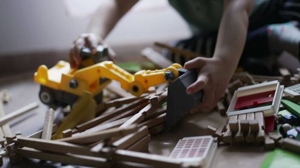 El niño juega con bulldozer tractor juguete recogiendo piezas de madera jugando en la sala de juegos en casa. Primer plano niño manos - Foto, Imagen