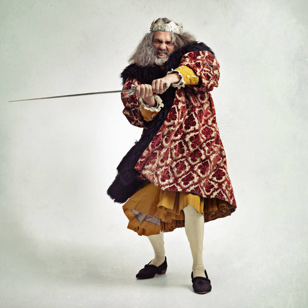 Man, royalty and portrait of king with sword in studio isolated on a gray background mock up. Vintage victorian, evil and mature mad male, angry ruler and leader holding blade for battle or fight - Foto, Imagem