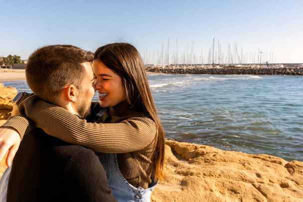 Optimistic young woman in casual clothes hugging and touching noses with man on rocky seashore on Saint Valentine Day - Foto, Imagem