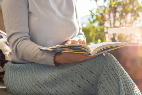 Женщина у окна в трикотажном свитере держит и читает книгу. Концепция расслабления. Закрыть - Фото, изображение