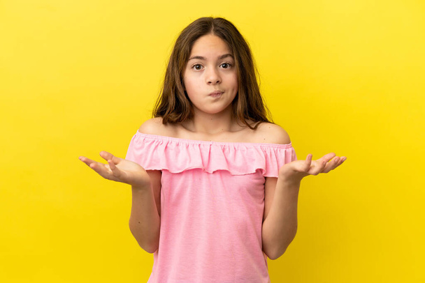 Little caucasian girl isolated on yellow background having doubts while raising hands - Photo, Image
