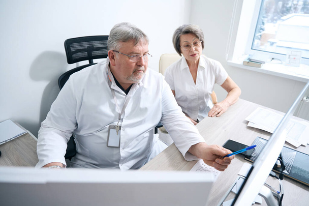Diagnostician consults an elderly patient in a hospital, modern equipment in the office - Photo, Image