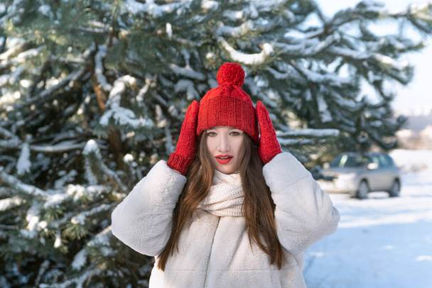 Portrait of beautiful young brunette woman in knitted red hat and mittens in winter park. Little Red Riding Hood - Foto, afbeelding