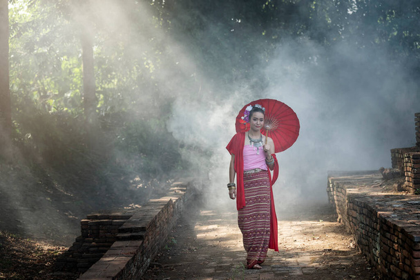 Hermosa mujer tailandesa vistiendo ropa tradicional tailandesa con paraguas rojo en medio del humo y la niebla. - Foto, Imagen