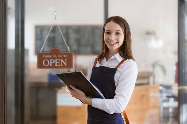 Young Female manager in restaurant with tablet. Woman coffee shop owner with open sign. Small business concept. - Foto, Imagem