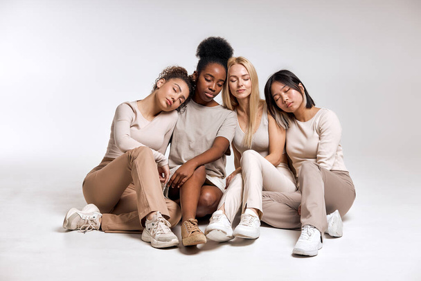Pacified different women sitting on floor in studio, enjoying friendship, leisure free time, close to each other. Models in stylish casual wear with natural hair and make-up. People lifestyle - Fotoğraf, Görsel